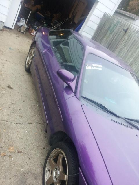 1995 Ford Probe - A purple Ford Probe is parked on a concrete driveway in front of an open garage. The car is viewed from the side at an angle, showing the f…