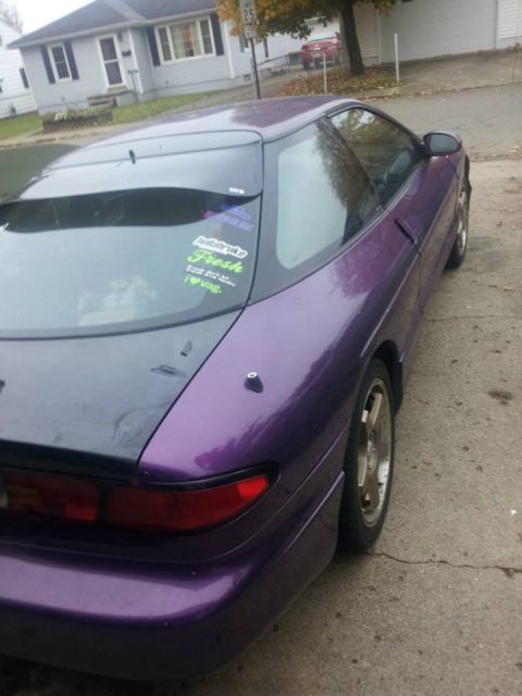1995 Ford Probe - The rear driver's side quarter panel of a purple 1995 Ford Probe is shown parked on a cracked concrete driveway. Several stickers are visib…