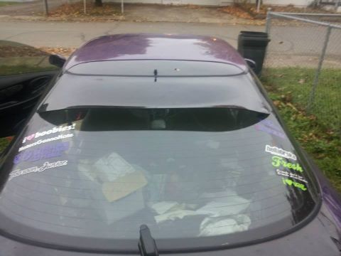 1995 Ford Probe - The rear windshield of a purple 1995 Ford Probe, nicknamed "Starscream", is covered in various stickers. Visible stickers include "i ❤️ boo…