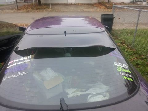 1995 Ford Probe - The rear windshield of a purple car is covered in stickers. Visible text includes "i❤boobies! HatersGonnaHate", "Toosoon Junior", and "hell…