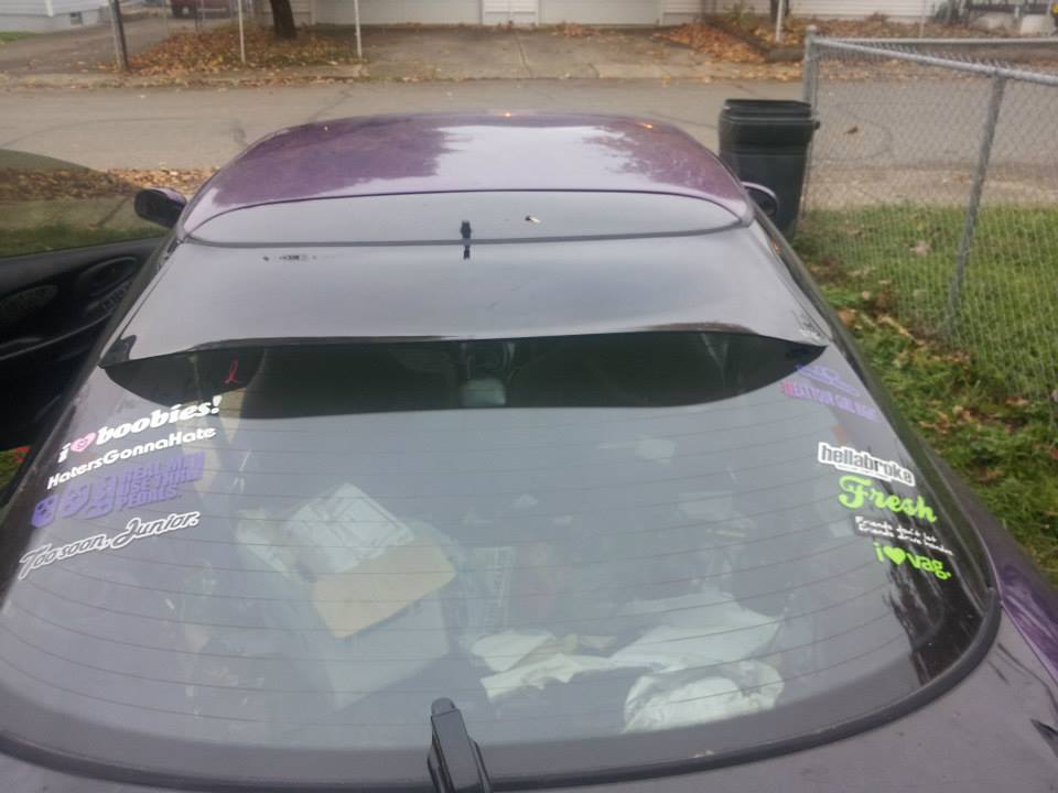 Rear windshield of a purple car with multiple stickers.