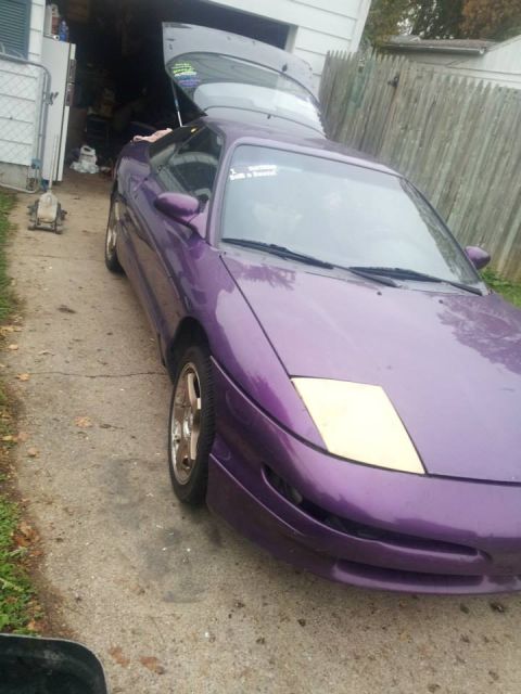 1995 Ford Probe - A purple 1995 Ford Probe with its trunk open is parked on a concrete driveway next to a wooden fence. A sticker is visible on the windshiel…