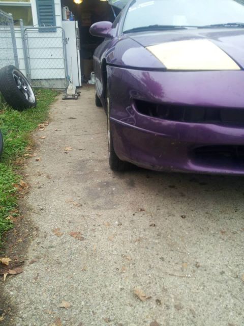 1995 Ford Probe - A low-angle, close-up view of the front right side of a purple sports coupe parked on a concrete driveway. A detached tire and a car jack a…
