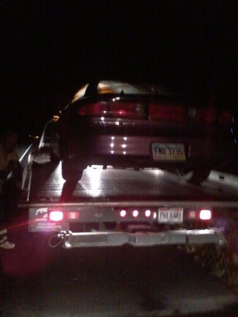1995 Ford Probe - The rear of a dark colored coupe is loaded onto a tow truck at night. The vehicle has a license plate that reads "FHO 3735".
