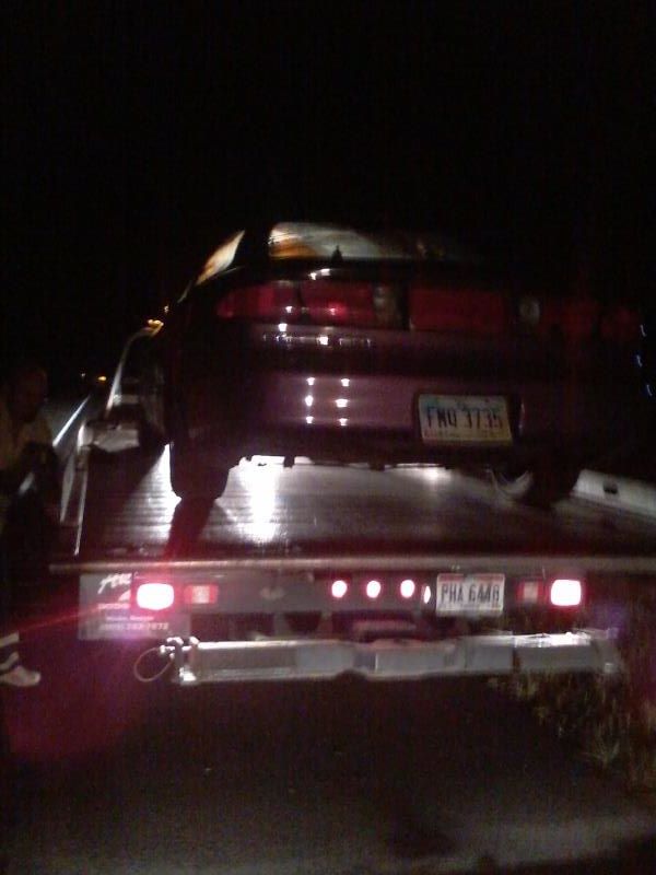 Dark coupe on a tow truck at night, rear view, license plate FHO 3735 visible.