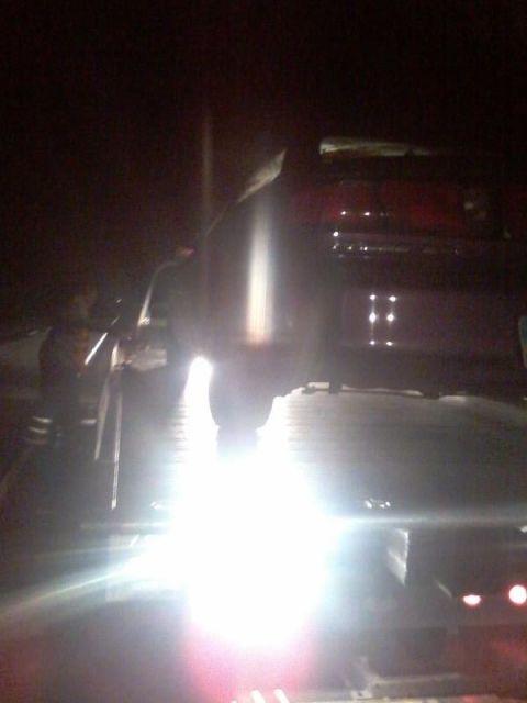 1995 Ford Probe - A red vehicle is loaded onto a tow truck at night. Bright lights illuminate the scene, obscuring some details of the vehicle's front.