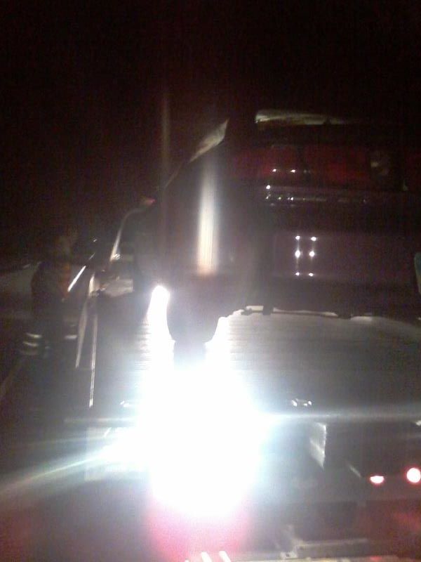 Red vehicle being loaded onto a tow truck at night, front obscured by bright lights.