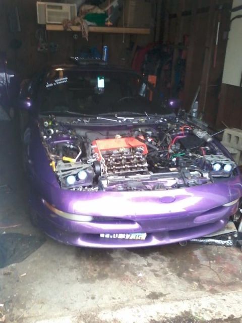 1995 Ford Probe - A purple Ford Probe is parked in a garage with its hood open, revealing the engine. The car has a custom license plate visible on the front…