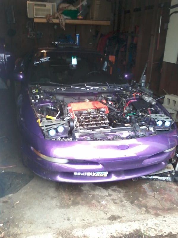 Purple Ford Probe with hood open in a garage, showing engine and custom license plate.