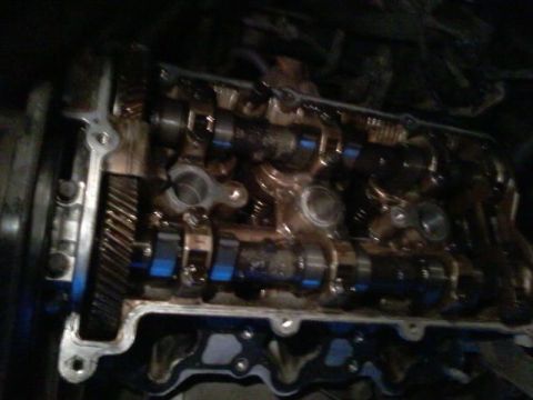1995 Ford Probe - Close-up view of the camshafts and timing gears within an engine's cylinder head. The metallic components are coated in oil, with some blue…