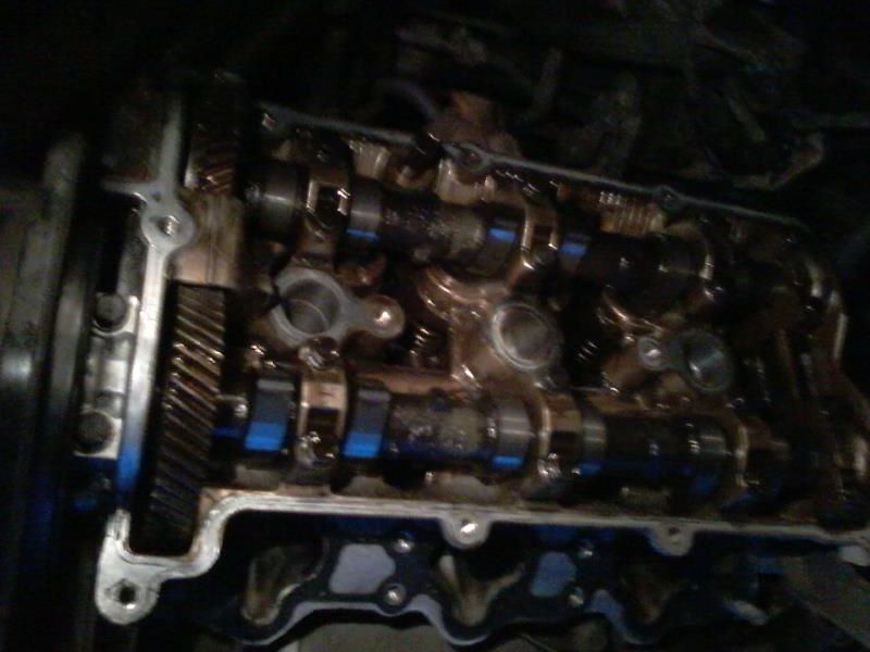 Engine cylinder head with camshafts and timing gears, showing oil and blue markings.