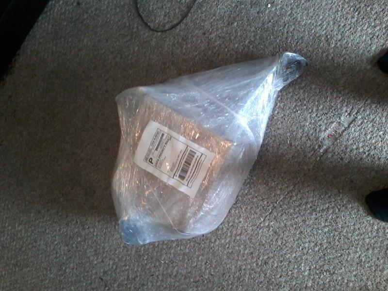 A package wrapped in plastic wrap on a carpeted floor.