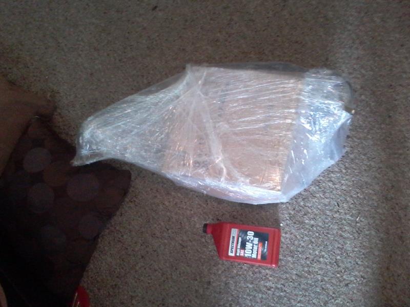 Bottle of motor oil on carpet next to a plastic-wrapped package.