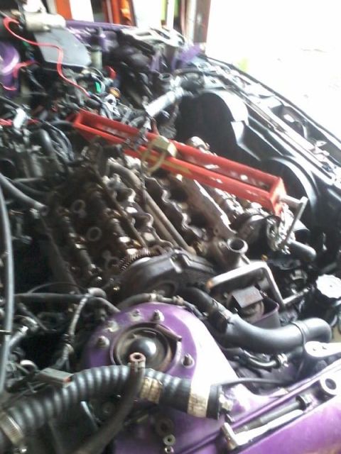 1995 Ford Probe - The engine bay of a purple 1995 Ford Probe is shown, with various engine components and wiring visible. A red engine hoist is positioned ab…