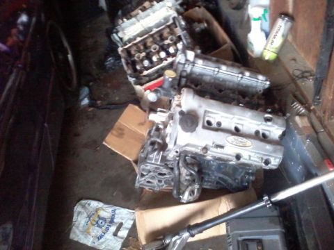 1995 Ford Probe - Two disassembled Ford engine blocks are shown on a cluttered floor, possibly in a garage or workshop. One engine block has a visible Ford l…