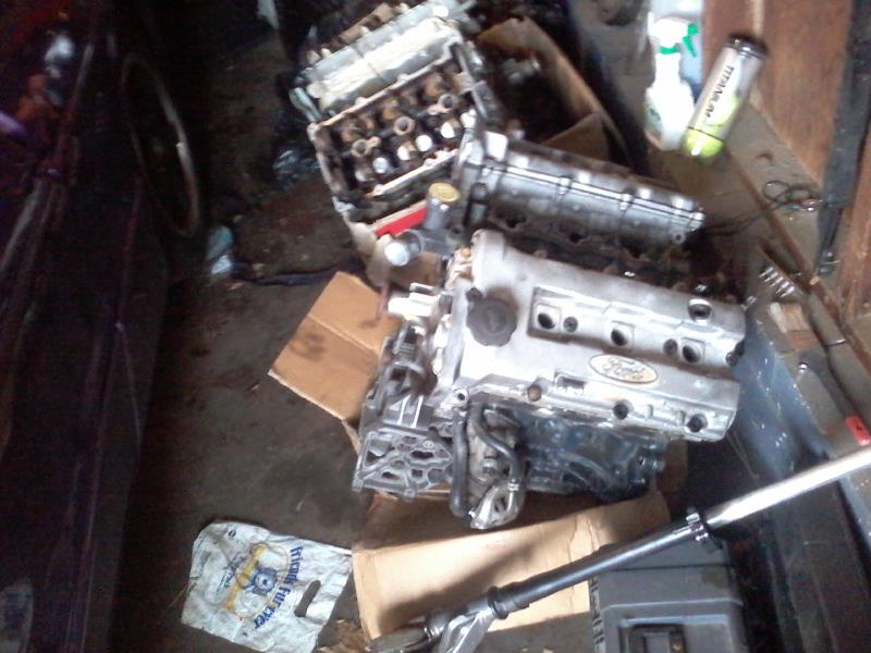 Two disassembled Ford engine blocks on a cluttered floor. One has a Ford logo.