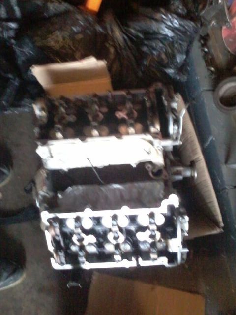 1995 Ford Probe - Two engine cylinder heads are stacked on top of each other and resting on cardboard. The cylinder heads appear to be from a 4-cylinder engi…