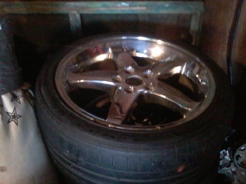 1995 Ford Probe - A chrome five-spoke aftermarket wheel is mounted on a tire, resting against a white bag with black stars. The wheel and tire are in a dimly…