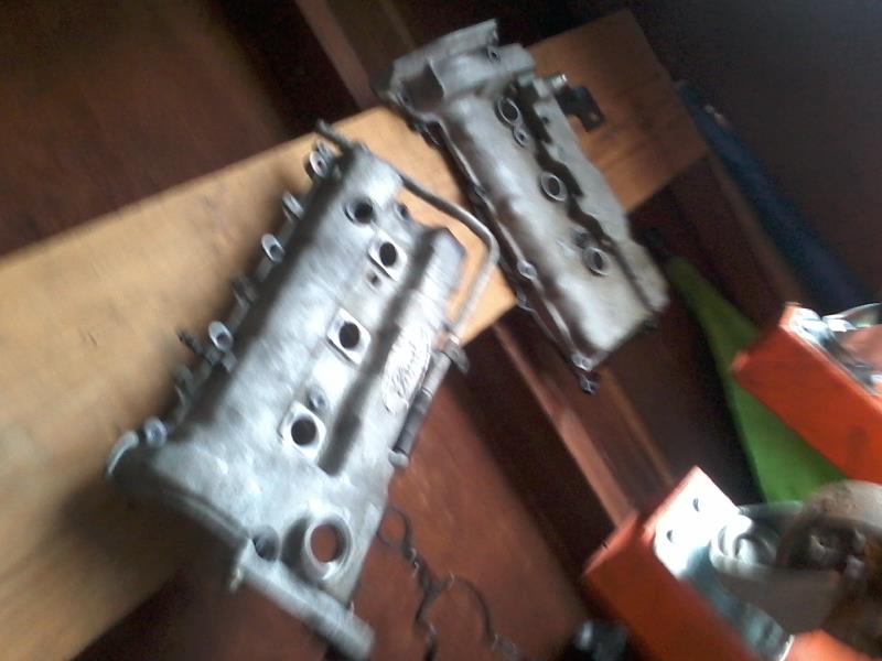 Two silver Ford valve covers on a wooden surface.