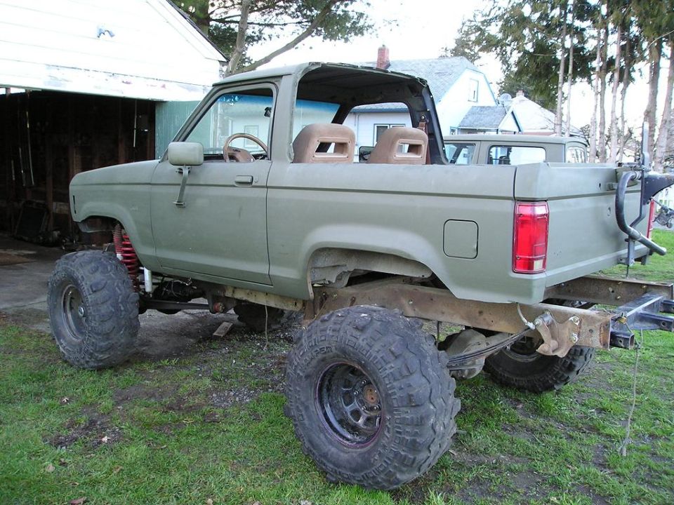 Olive-green lifted Bronco II, topless, on large mud tires, rear side view