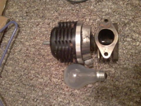 1995 Ford Probe - A turbocharger wastegate and a lightbulb are placed on a carpeted surface. The wastegate is black and silver with a metal flange attached.
