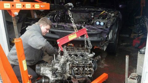 1995 Ford Probe - A person is working on removing a car engine using an engine hoist. The engine is suspended by chains and a red engine support bar, with th…