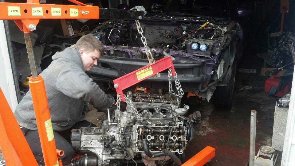 Person removing a car engine with an engine hoist.