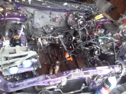 1995 Ford Probe - The engine bay of a purple 1995 Ford Probe is shown with the engine removed, revealing the chassis and various wiring harnesses and plumbin…