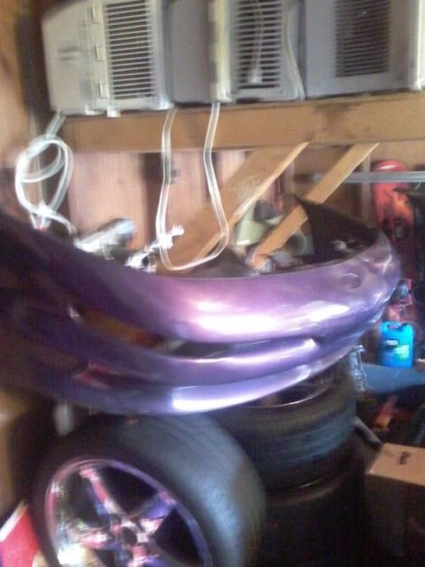 1995 Ford Probe - A purple car bumper is stacked on top of tires in a garage setting. Two window air conditioning units are visible above the bumper.