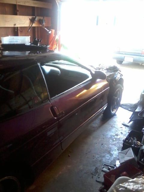 1995 Ford Probe - A dark red coupe is parked in a garage with the hood open, revealing engine components. Various tools and parts are scattered on the concre…