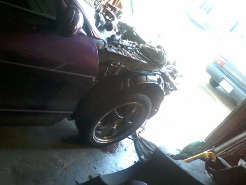 1995 Ford Probe - The front passenger side of a damaged purple car is shown, with the fender and hood significantly compromised. A second dark-colored car is…