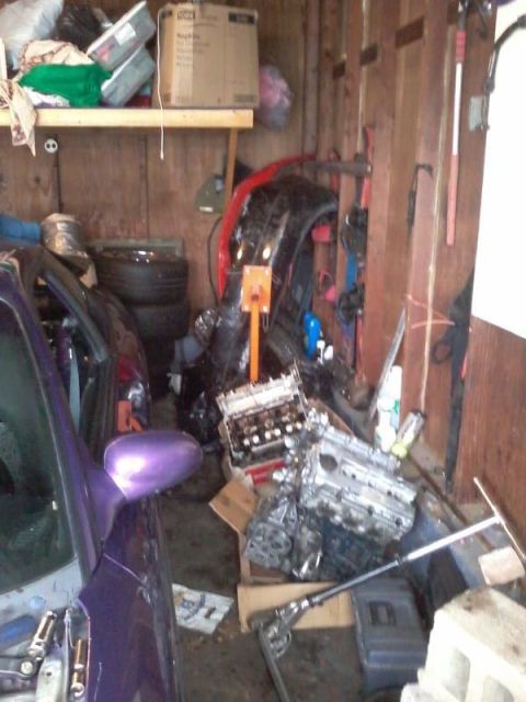 1995 Ford Probe - A partially disassembled car with a purple body is parked in a cluttered garage. Various car parts, including an engine and a bumper, are s…
