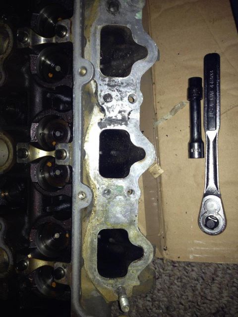 1995 Ford Probe - A close-up view of a disassembled engine cylinder head with intake ports and a gasket, alongside a socket wrench and a socket extension. Th…