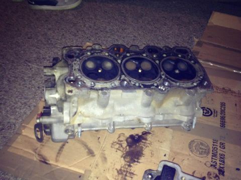 1995 Ford Probe - A close-up, angled view of a disassembled engine cylinder head with visible valves. The part is resting on a cardboard surface with some oi…