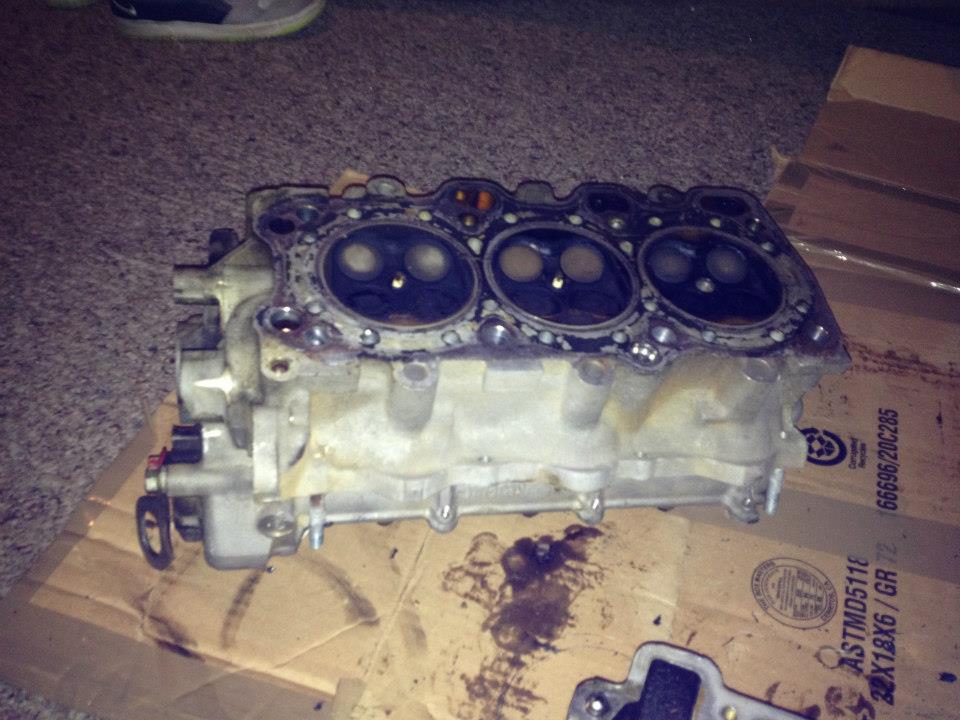 Disassembled engine cylinder head with valves visible, resting on stained cardboard.