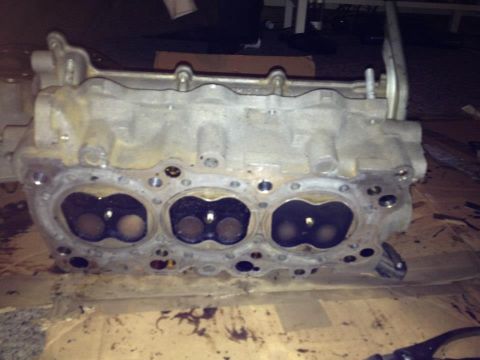 1995 Ford Probe - A close-up view of a disassembled engine cylinder head, showing the intake and exhaust ports. The aluminum casting is dirty and shows signs…