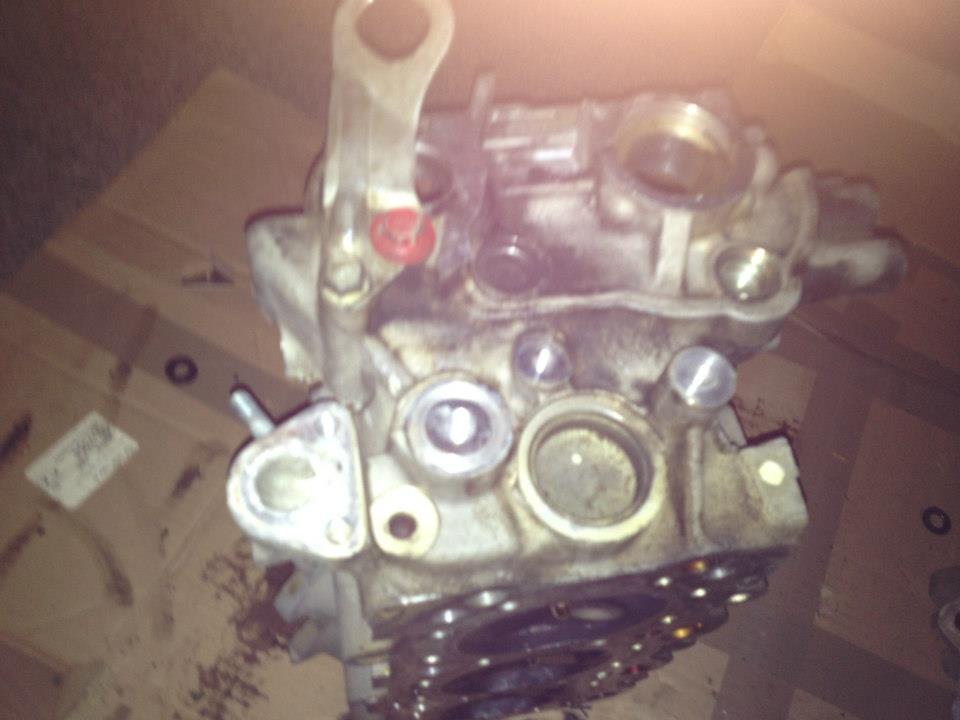 Disassembled engine cylinder head with bolts and ports, overhead view.