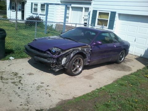 1995 Ford Probe - A purple Ford Probe with its front end damaged and partially disassembled sits in a driveway in front of a white garage.