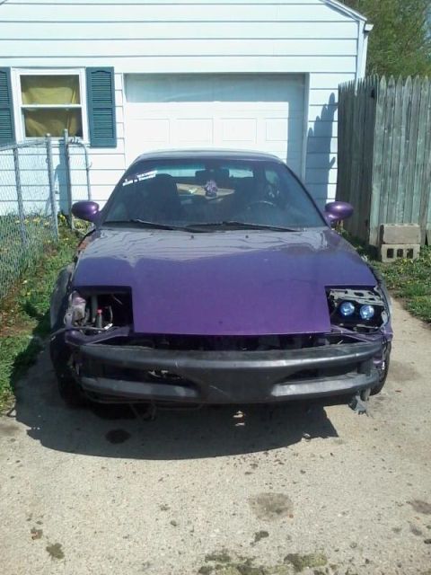1995 Ford Probe - The front view of a modified purple 1995 Ford Probe is parked in a driveway in front of a garage. The car has a damaged front bumper and mi…