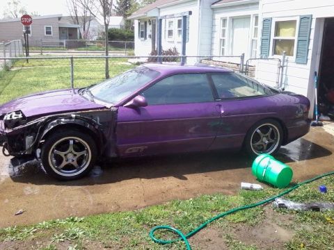1995 Ford Probe - A purple Ford Probe GT is parked on a wet driveway with its front fender removed, revealing the wheel well and engine components. A green b…