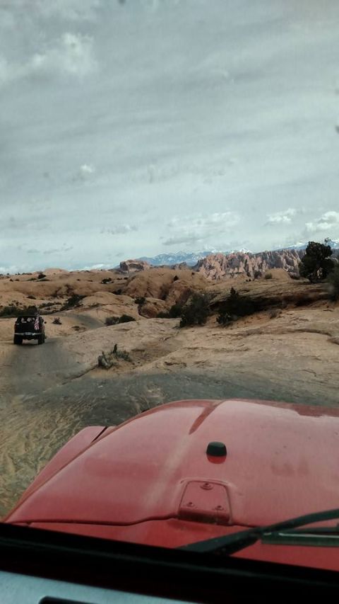 1979 Ford Bronco - A red Jeep Wrangler is driving on a rocky, off-road trail with another black Jeep in the distance. The landscape features sandstone formati…