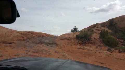1979 Ford Bronco - The hood and windshield frame of a vehicle are visible in the foreground, looking out at a desert landscape with red rock formations and sp…