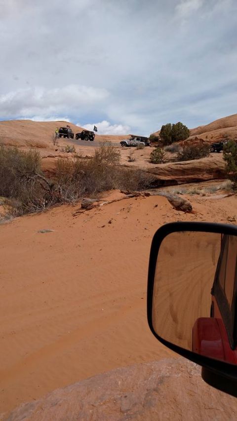 1979 Ford Bronco - A group of off-road vehicles, including Jeeps, are driving on a sandy trail in a desert landscape under a cloudy sky. The photo is taken fr…