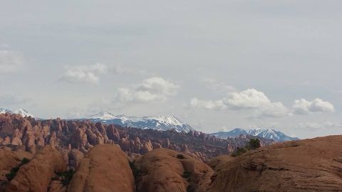 1979 Ford Bronco - A wide landscape shot shows dramatic red rock formations in the foreground and middle ground, with snow-capped mountains visible in the dis…