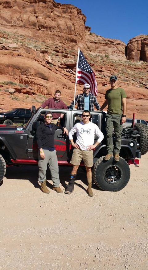 1979 Ford Bronco - Five men pose with an American flag in front of a dark gray Jeep Wrangler with red accents in a desert landscape.