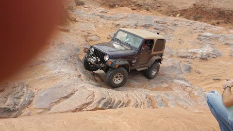 1979 Ford Bronco - A dark blue Jeep Wrangler is navigating a rocky, off-road trail. The vehicle is angled on a steep incline with large tires gripping the ter…