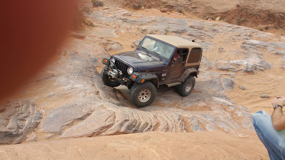 Dark blue Jeep Wrangler driving on a rocky off-road trail.