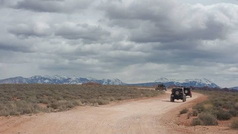 1979 Ford Bronco - Three Jeep Wranglers drive down a dirt road in a desert landscape with snow-capped mountains in the background.