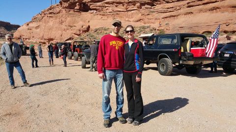1979 Ford Bronco - A man and woman pose in front of a black Ford Bronco with an American flag in the bed, parked in a desert landscape with other off-road veh…