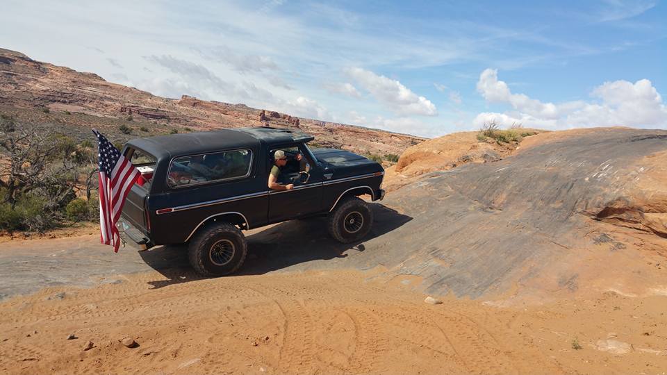 Black lifted Ford Bronco driving on a rocky desert trail with an American flag.